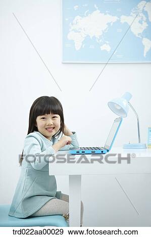Stock Photo - A smiling girl with a laptop on the desk. Fotosearch
