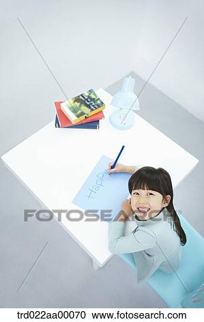 Stock Image - A smiling girl writing 'Happy' on the blue paper with a blue colored pencil. Fotosearch