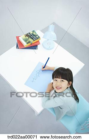 Stock Image - A smiling girl writing 'Happy' on the blue paper with a blue colored pencil. Fotosearch
