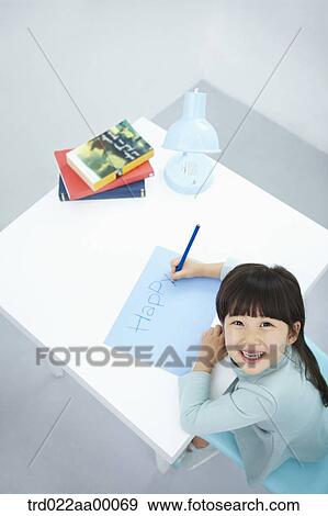 Stock Photo - A smiling girl writing 'Happy' on the blue paper with a blue colored pencil. Fotosearch