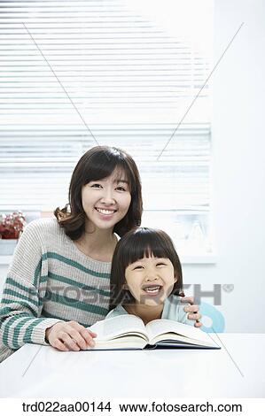 Picture - A smiling woman and girl with a book on the desk. Fotosearch