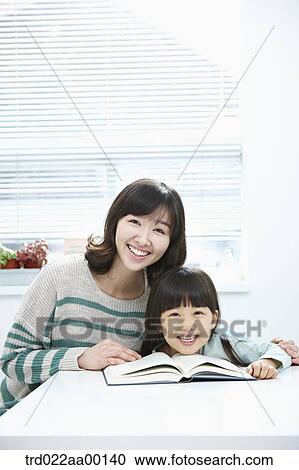 Stock Image - A smiling woman and girl with a book on the desk. Fotosearch