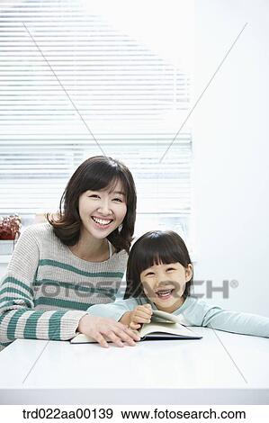 A smiling woman and girl with a book on the desk View Large Photo Image Stock Photo - A smiling woman and girl with a book on the desk. Fotosearch