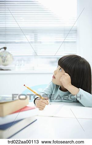 Stock Image - A thinking girl while holding a pencil over a note book. Fotosearch