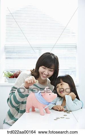 A woman and girl putting a coin into a pink piggy bank View Large Photo Image Picture - A woman and girl putting a coin into a pink piggy bank. Fotosearch
