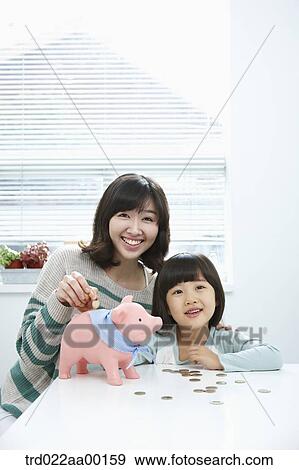 Stock Photo - A woman and girl putting a coin into a pink piggy bank. Fotosearch
