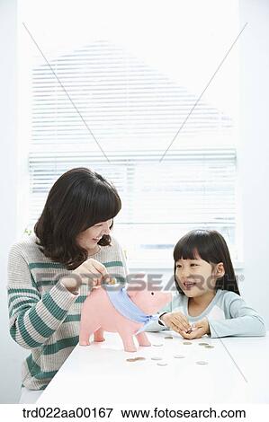 A woman and girl putting a coin into a pink piggy bank View Large Photo Image Stock Photo - A woman and girl putting a coin into a pink piggy bank. Fotosearch