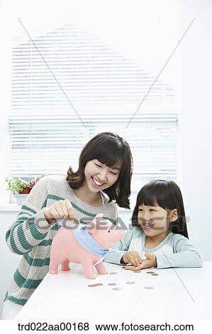 Stock Photo - A woman and girl putting a coin into a pink piggy bank. Fotosearch