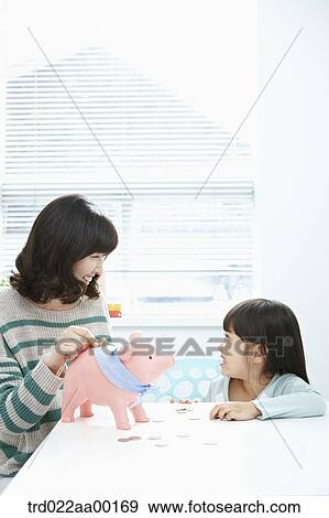 Stock Photo - A woman and girl putting a coin into a pink piggy bank. Fotosearch