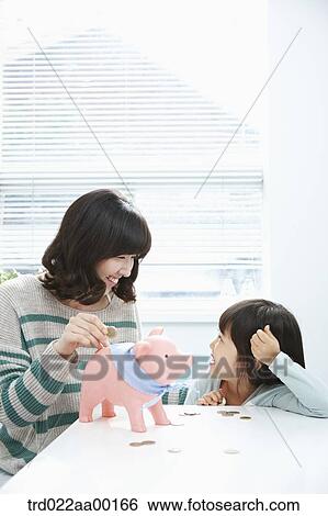 Stock Photograph - A woman and girl putting a coin into a pink piggy bank. Fotosearch