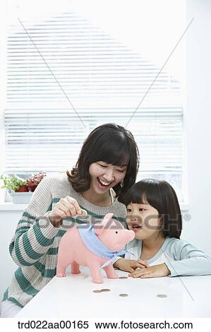 Stock Photography - A woman and girl putting a coin into a pink piggy bank. Fotosearch