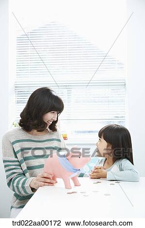 A woman and girl smiling at each other with a pink piggy bank and coin on the desk View Large Photo Image Stock Image - A woman and girl smiling at each other with a pink piggy bank and coin on the desk. Fotosearch