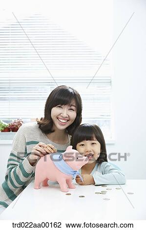 Stock Image - A woman and girl with a pink piggy bank and coin on the desk. Fotosearch