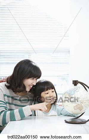 Stock Image - A woman pointing to a globe and girl looking at a globe. Fotosearch