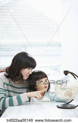 Stock Photo - A woman pointing to a globe and girl looking at a globe. Fotosearch