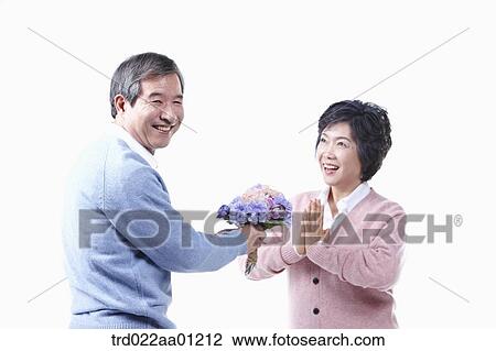Stock Image - An elderly man giving a bouquet of flower for an elderly woman . Fotosearch