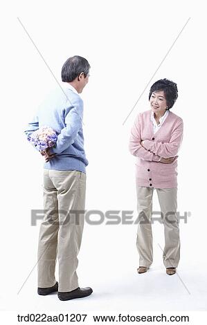 Stock Photo - An elderly man hiding a bouquet of flower for an elderly woman . Fotosearch