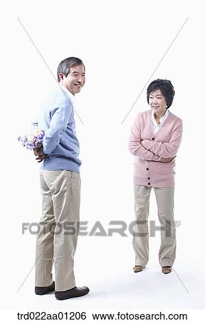 Stock Photograph - An elderly man hiding a bouquet of flower for an elderly woman . Fotosearch