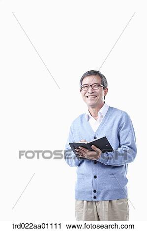 Stock Image - An elderly man holding a pen and planner in glasses. Fotosearch