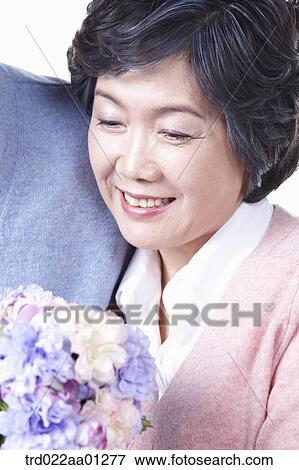 Stock Photo - An smiling elderly woman looking at a bouquet of flower. Fotosearch