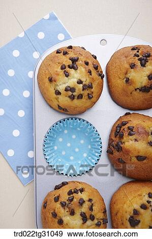 Stock Photo - The chocolate chip muffin and blue baking cup in the baking mold. Fotosearch