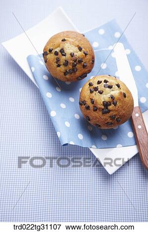Stock Photo - The chocolate chip muffin served on the dish with the blue napkin and knife. Fotosearch
