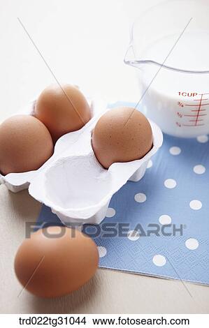 Picture - The eggs in the carton and a cup of milk on the blue polka dots napkin. Fotosearch