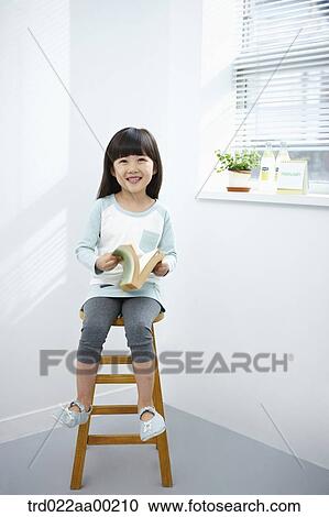 The girl holding a book on the chair View Large Photo Image Stock Image - The girl holding a book on the chair. Fotosearch