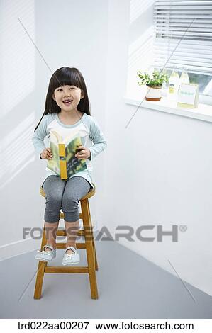 The girl holding a book on the chair View Large Photo Image Stock Photo - The girl holding a book on the chair. Fotosearch