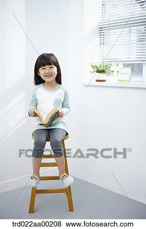 Stock Photo - The girl holding a book on the chair. Fotosearch