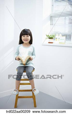 The girl holding a book on the chair View Large Photo Image Stock Photo - The girl holding a book on the chair. Fotosearch