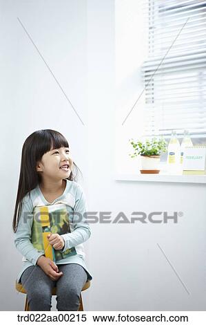 Stock Photography - The girl holding a book on the chair. Fotosearch