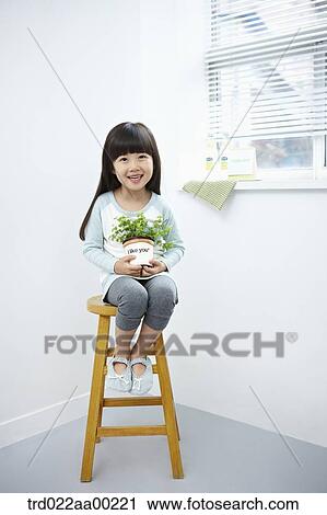 The girl holding the green plant pot on the chair View Large Photo Image Stock Image - The girl holding the green plant pot on the chair. Fotosearch