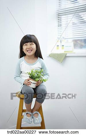 The girl holding the green plant pot on the chair View Large Photo Image Stock Photo - The girl holding the green plant pot on the chair. Fotosearch