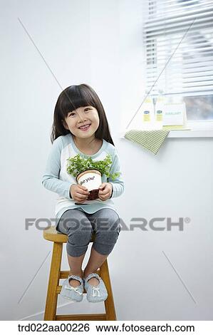 Stock Photograph - The girl holding the green plant pot on the chair. Fotosearch