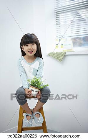 Stock Photography - The girl holding the green plant pot on the chair. Fotosearch