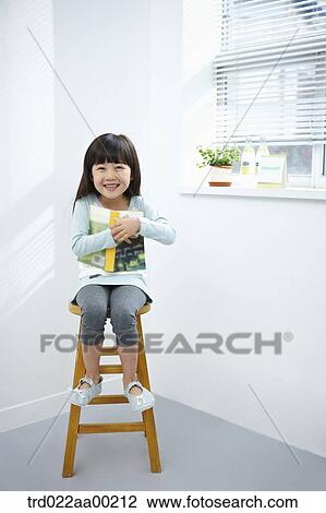 Stock Image - The girl hugging a book on the chair. Fotosearch