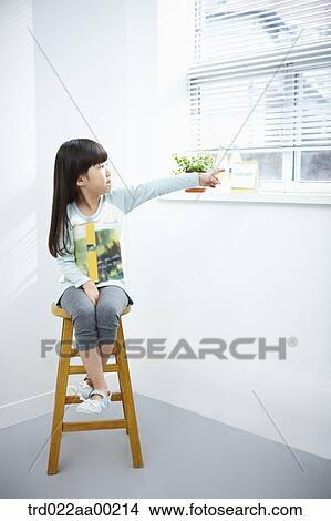 Picture - The girl pointing out the window on the chair. Fotosearch