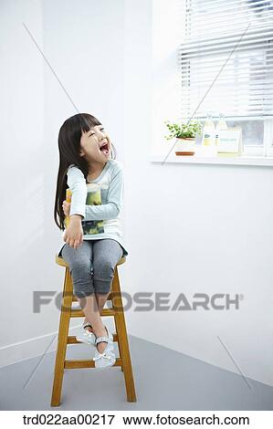 Stock Photo - The girl with big smile holding a book on the chair . Fotosearch