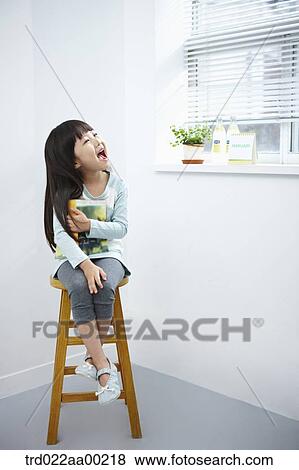 The girl with big smile holding a book on the chair View Large Photo Image Stock Photo - The girl with big smile holding a book on the chair . Fotosearch