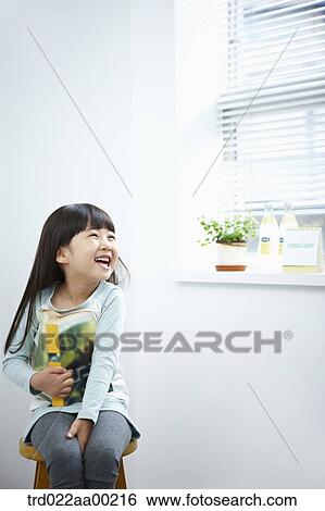 Stock Photograph - The girl with big smile holding a book on the chair . Fotosearch