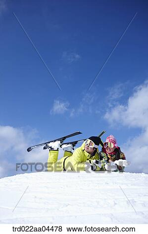 Stock Photo - The man and woman lying on the slope with the sky gear . Fotosearch