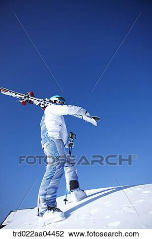 Stock Image - The man wearing skiwear with the ski boards on his shoulder. Fotosearch