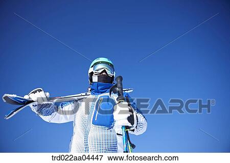 Stock Photo - The man wearing skiwear with the ski poles and ski boards. Fotosearch