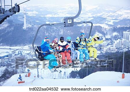 Stock Image - The people wearing the ski and snowboarding gear on the lift. Fotosearch