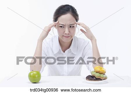 Stock Photograph - The stressful woman with an apple and doughnuts. Fotosearch
