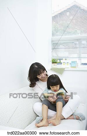 Stock Image - The woman and girl reading a book together. Fotosearch