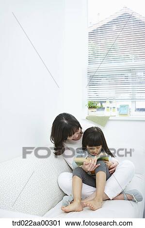 Stock Image - The woman and girl reading a book together. Fotosearch