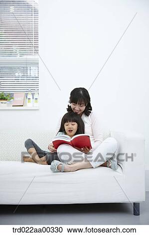 Stock Image - The woman and girl reading a book together on the couch. Fotosearch
