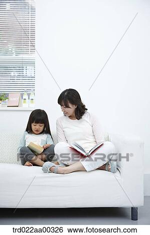 The woman and girl reading a book together on the couch View Large Photo Image Stock Photograph - The woman and girl reading a book together on the couch. Fotosearch
